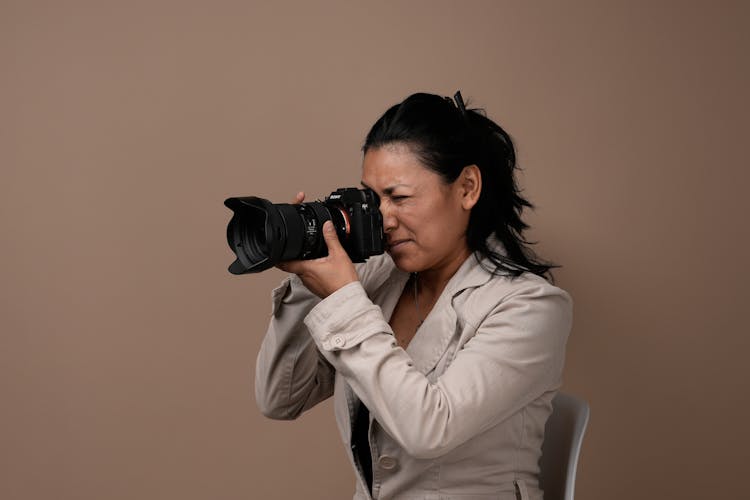 Woman Sitting On Chair In Studio Using Professional Camera