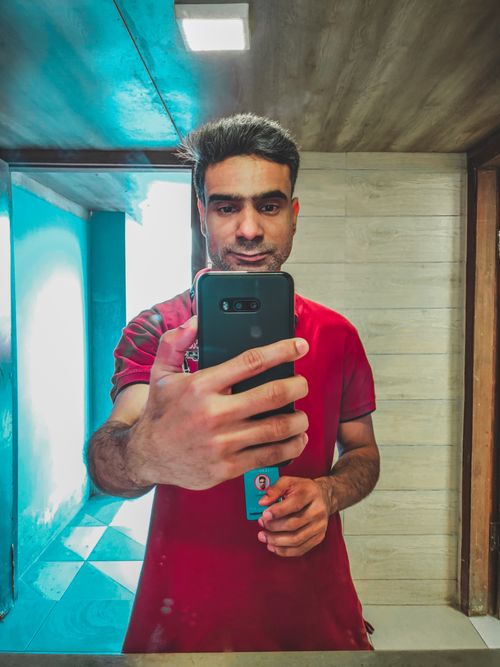 Free Adult man taking a selfie in a public bathroom mirror with a smartphone. Stock Photo