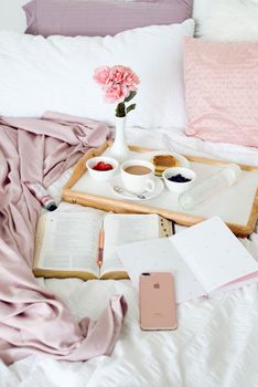 Comfortable bed setup with a breakfast tray, flowers, and pink decor for a relaxing morning.