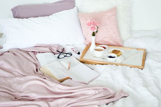Relaxing morning scene with breakfast in bed, books, flowers, and cozy bedding.