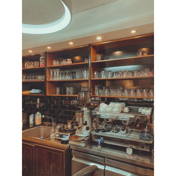 Stylish cafe interior featuring a coffee machine, grinder, and shelves filled with glasses and cups.