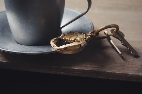 Free Close-up of a metallic crab keychain beside a cup on a wooden table. Stock Photo