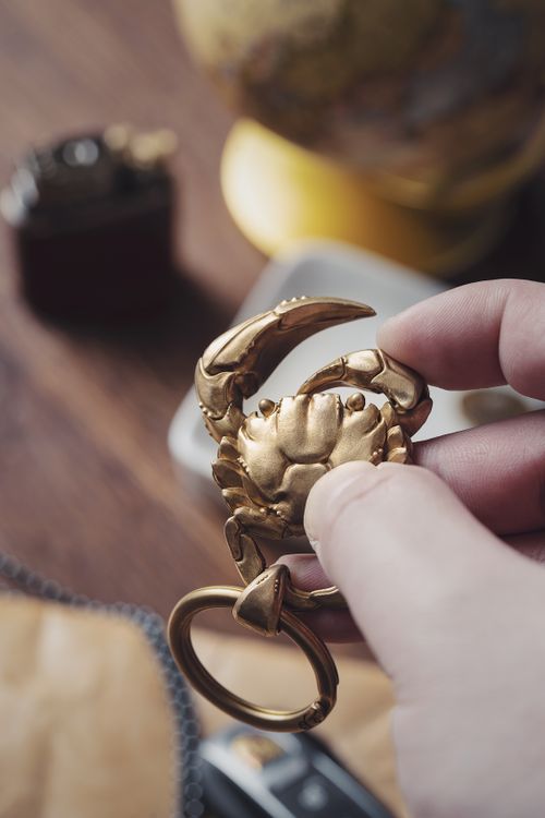 Free A close-up of a hand holding a golden crab-shaped key chain, captured indoors. Stock Photo