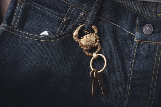 A close-up view of a golden crab keychain hanging from denim jeans. Stylish and unique accessory.