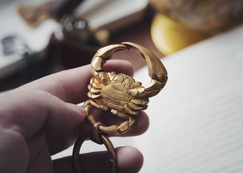 Free Closeup of a hand holding a golden crab shaped keychain, emphasizing detail and texture. Stock Photo