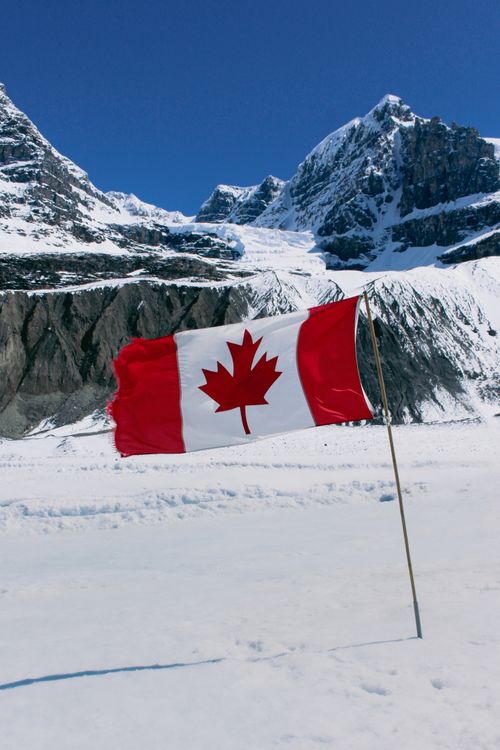 Free Iconic Canadian flag waves in the snowy Rocky Mountains of Jasper, Alberta. Stock Photo