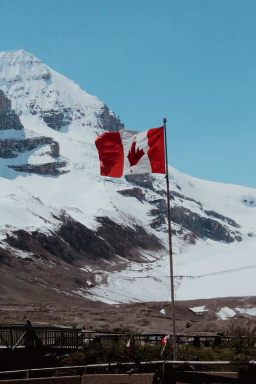 Free Canadian flag waving against a snow-covered mountain in a rural winter landscape. Stock Photo