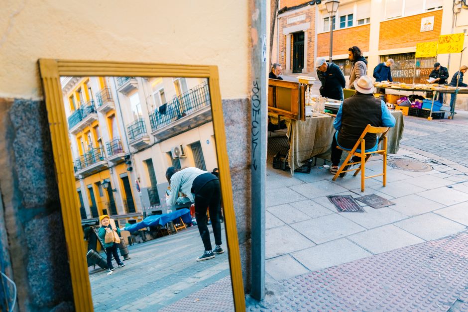 Escena de calle con un bullicioso mercado de pulgas y reflejo de un niño en el espejo.