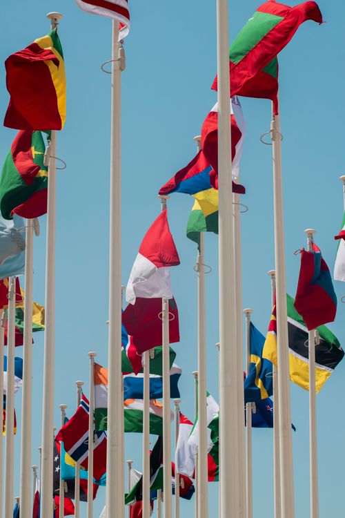 Free Vibrant display of international flags on tall flagpoles against a clear blue sky, symbolizing global unity. Stock Photo