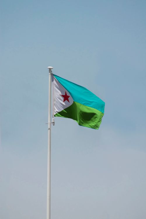 Free Photograph of the Djibouti national flag hoisted against a clear blue sky. Stock Photo