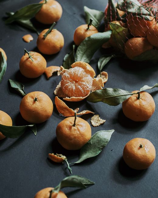 Scattered clementines and leaves on a dark surface, highlighting freshness and texture.