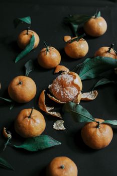 A collection of fresh clementines with vibrant green leaves on a dark surface, highlighting their juicy and natural appeal.