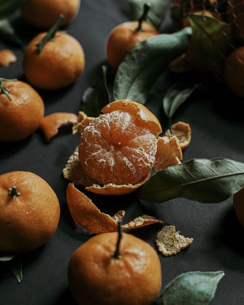 Free A still life image of fresh mandarins, both whole and peeled, scattered on a dark surface. Stock Photo