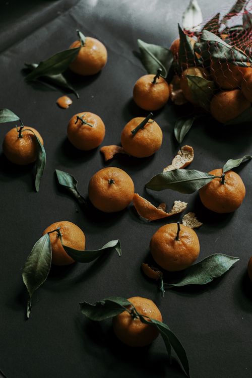 Free Ripe mandarins with green leaves spill across a dark surface, exuding freshness and natural harvest vibes. Stock Photo