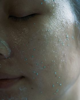 Close-up of a woman's face covered with a glittery, hydrating cosmetic face mask for skincare treatment.