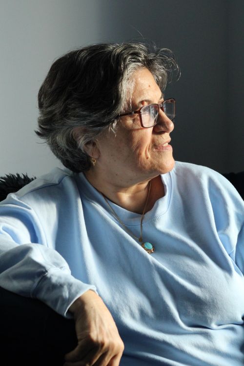 Free A senior woman in glasses and a blue sweater enjoying sunlight indoors. Stock Photo