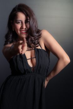 Confident woman in a stylish black dress posing with a smile in a studio setting.