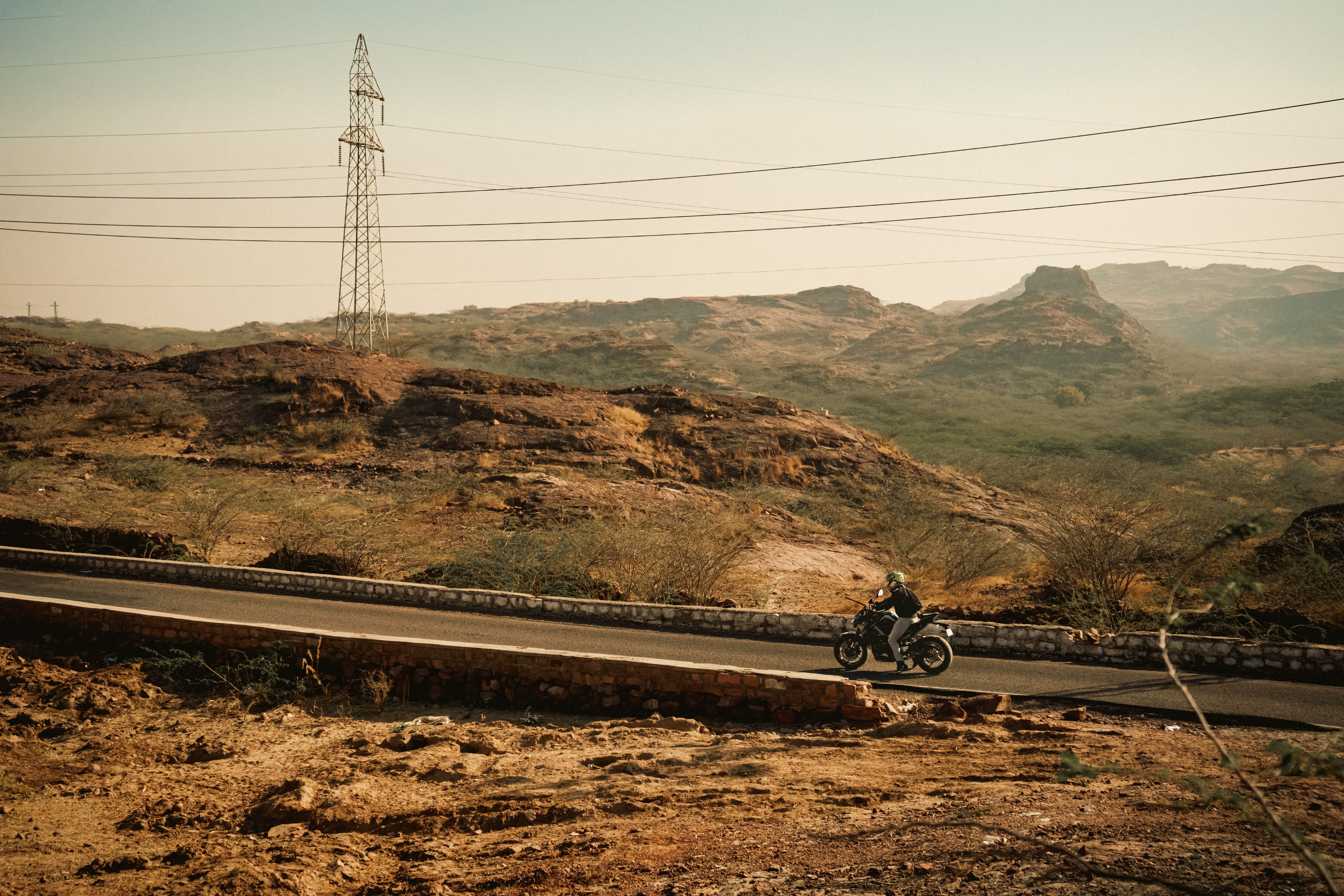 A lone motorcyclist rides through a rugged desert landscape under clear skies.