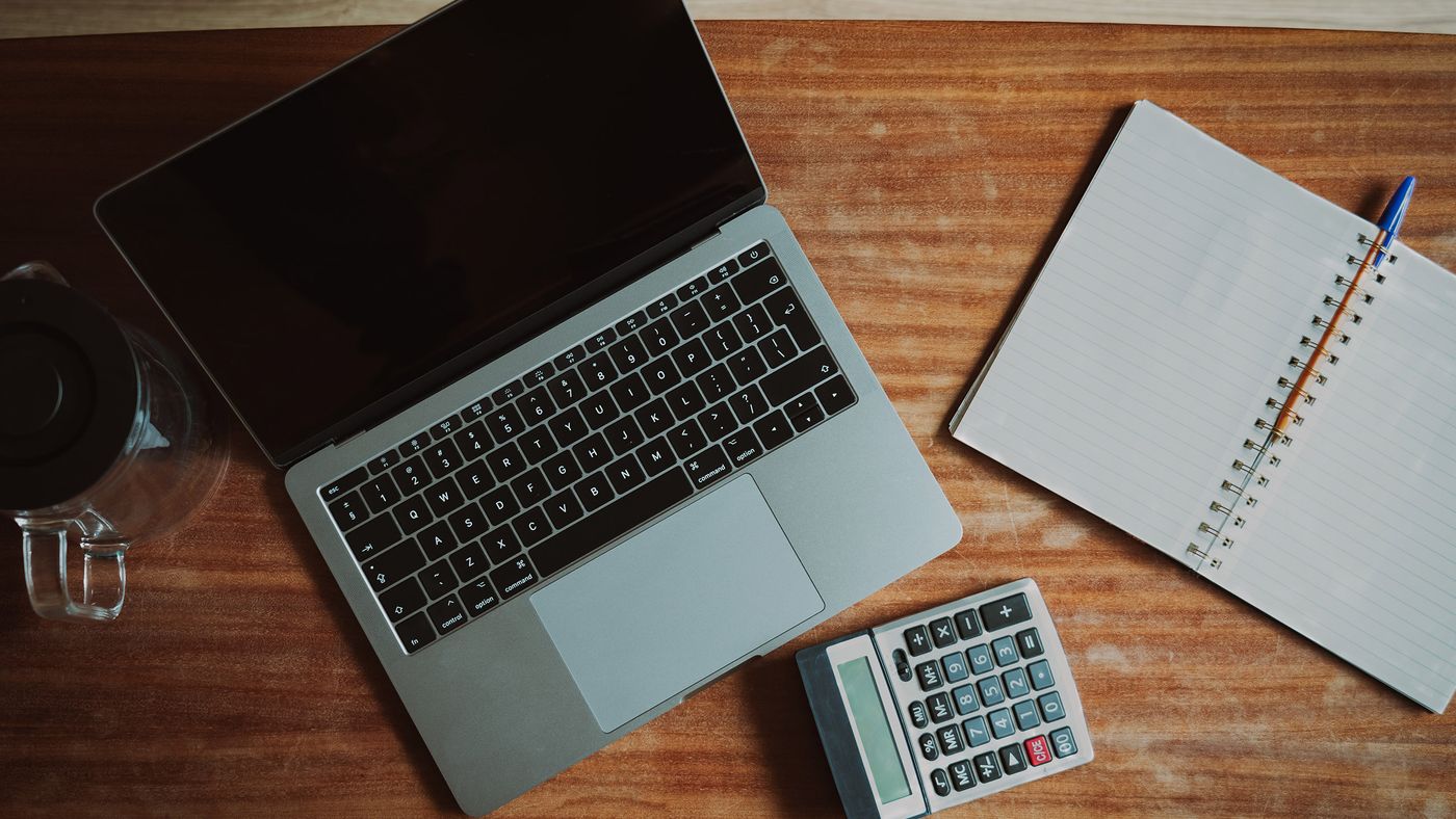 Identify the installed product before changing it. Photo: Jakub Zerdzicki / Pexels; illustrative workspace, not an Excel settings screenshot. Laptop with a blank screen beside a calculator and an open notebook on a wooden desk