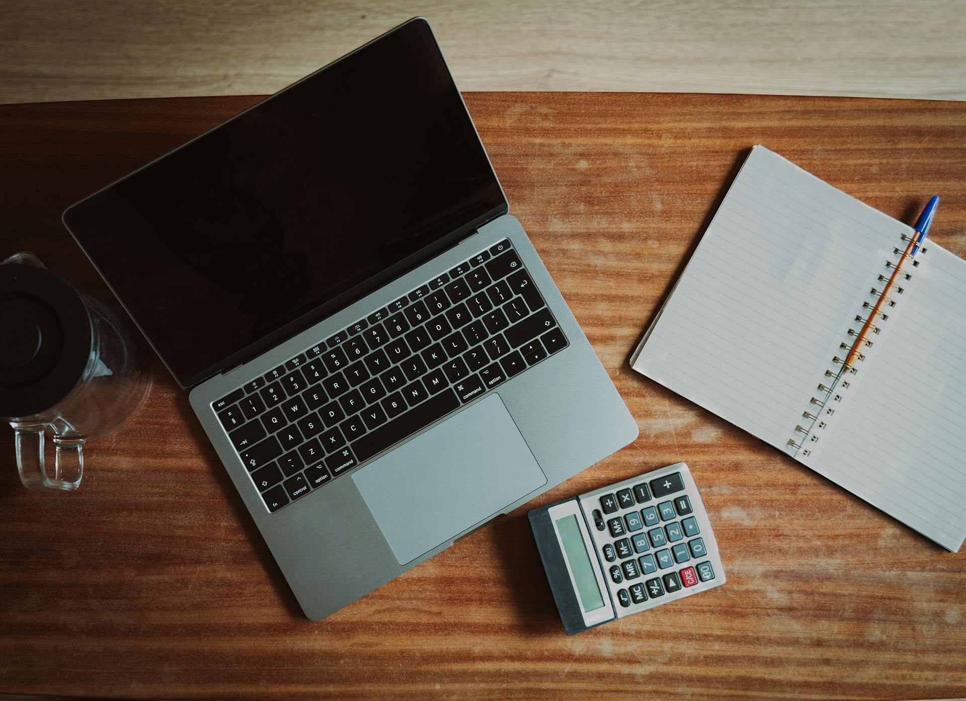 Top view of a desk with a laptop, calculator, and open notepad for work or study.