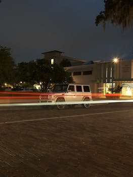 A long exposure captures an SUV at night in a parking lot with motion blur from passing lights.