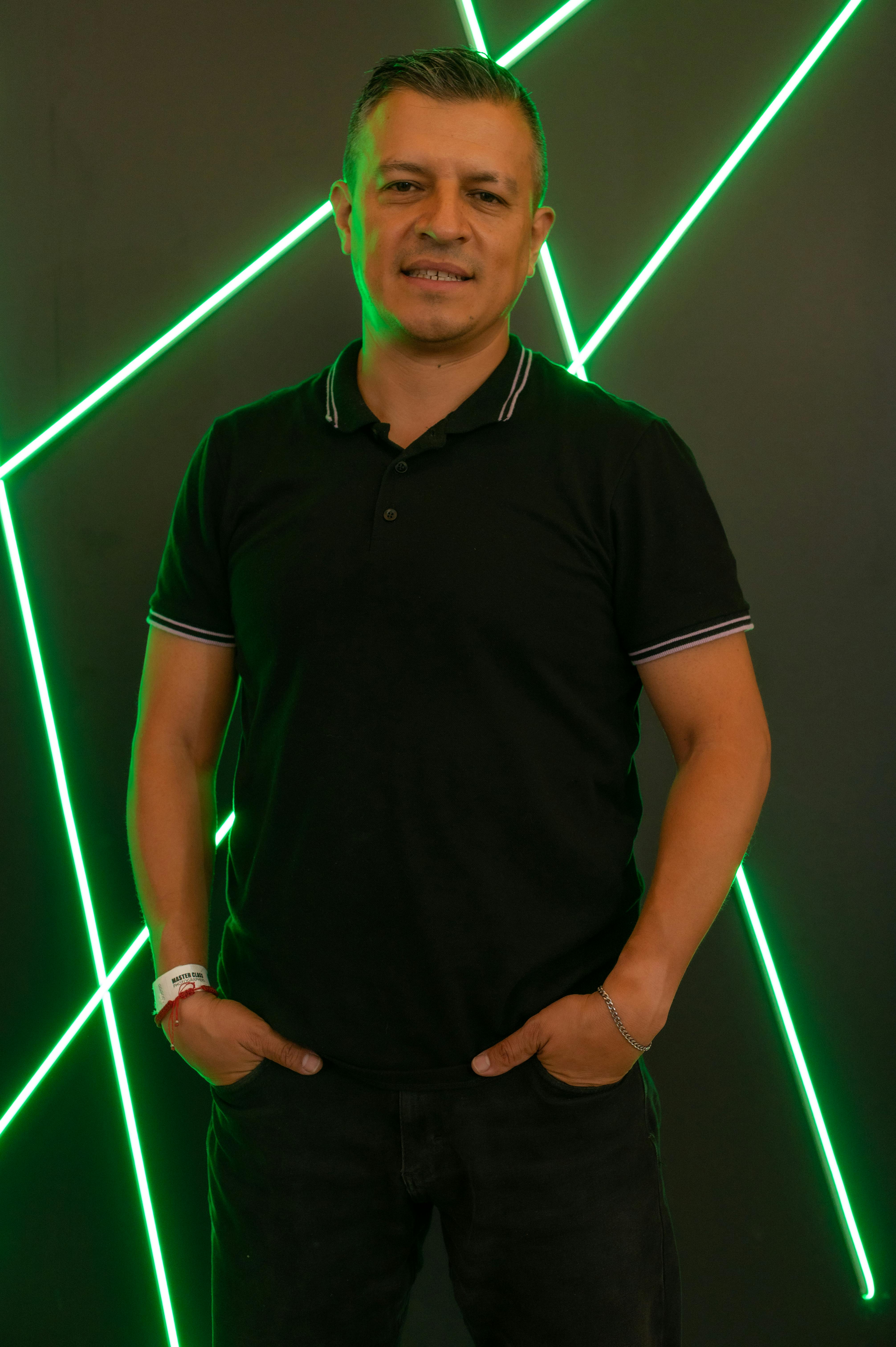 Man in black polo shirt posing with vibrant neon light backdrop.