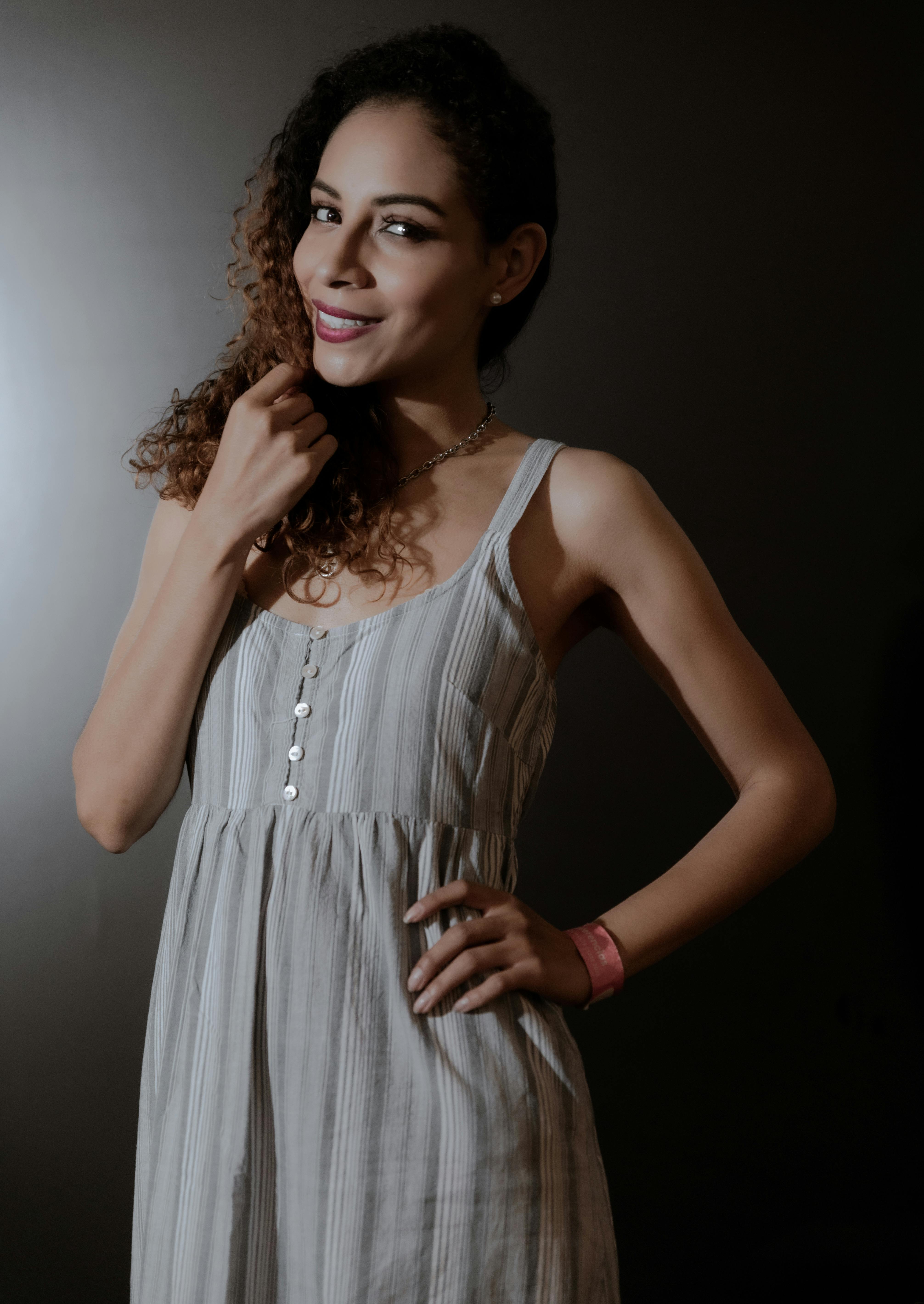 Fashionable studio portrait of a woman in a striped dress posing confidently against a dark background.