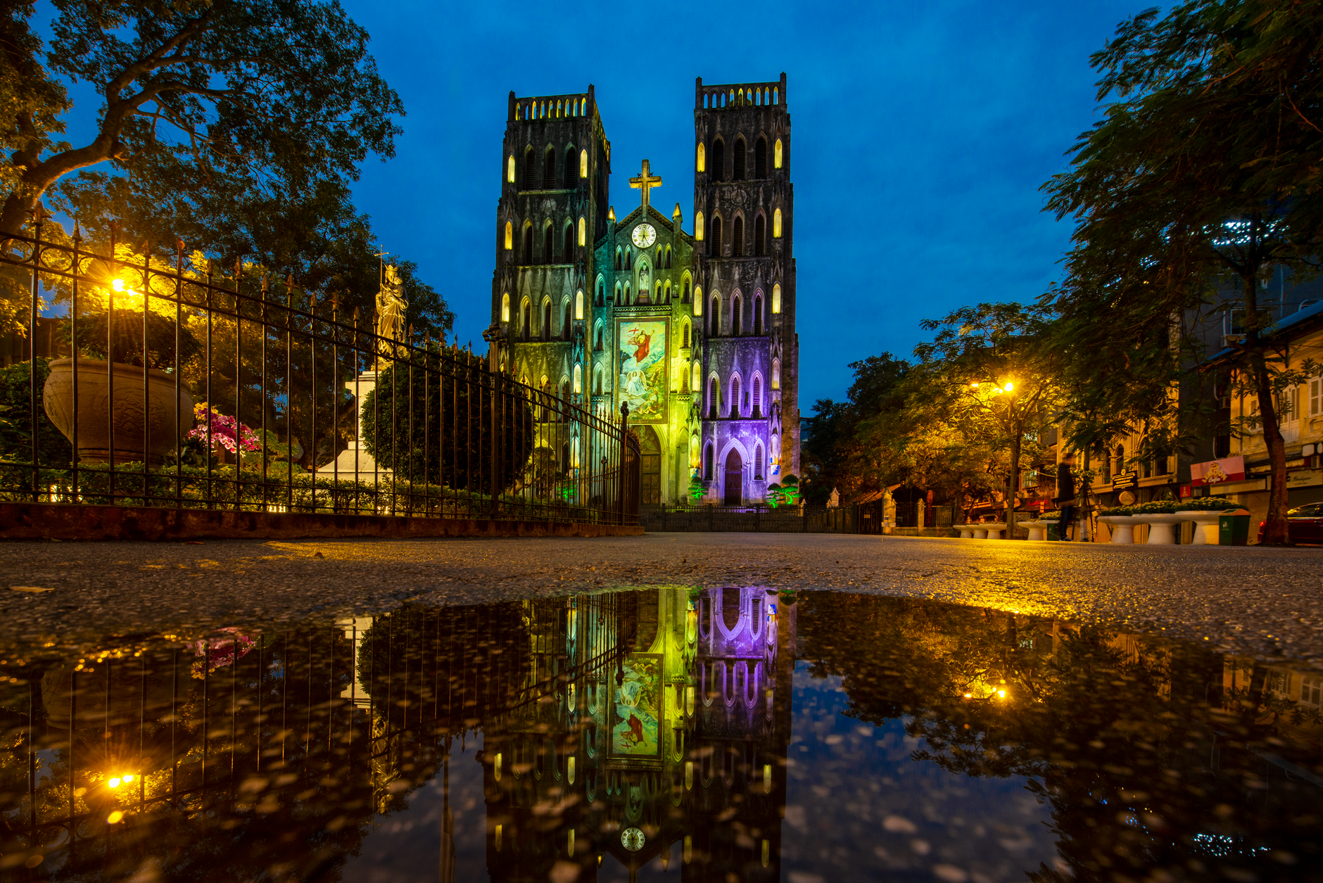 Beautiful cathedral facade glowing under night sky, reflected in a puddle.