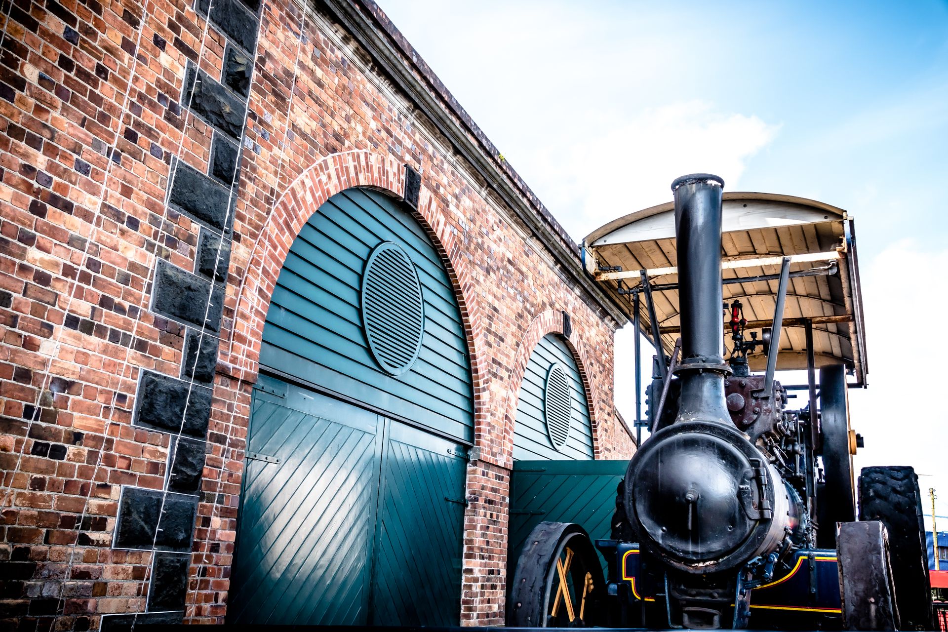 Historic steam engine parked alongside a vintage brick building in Auckland, New Zealand.