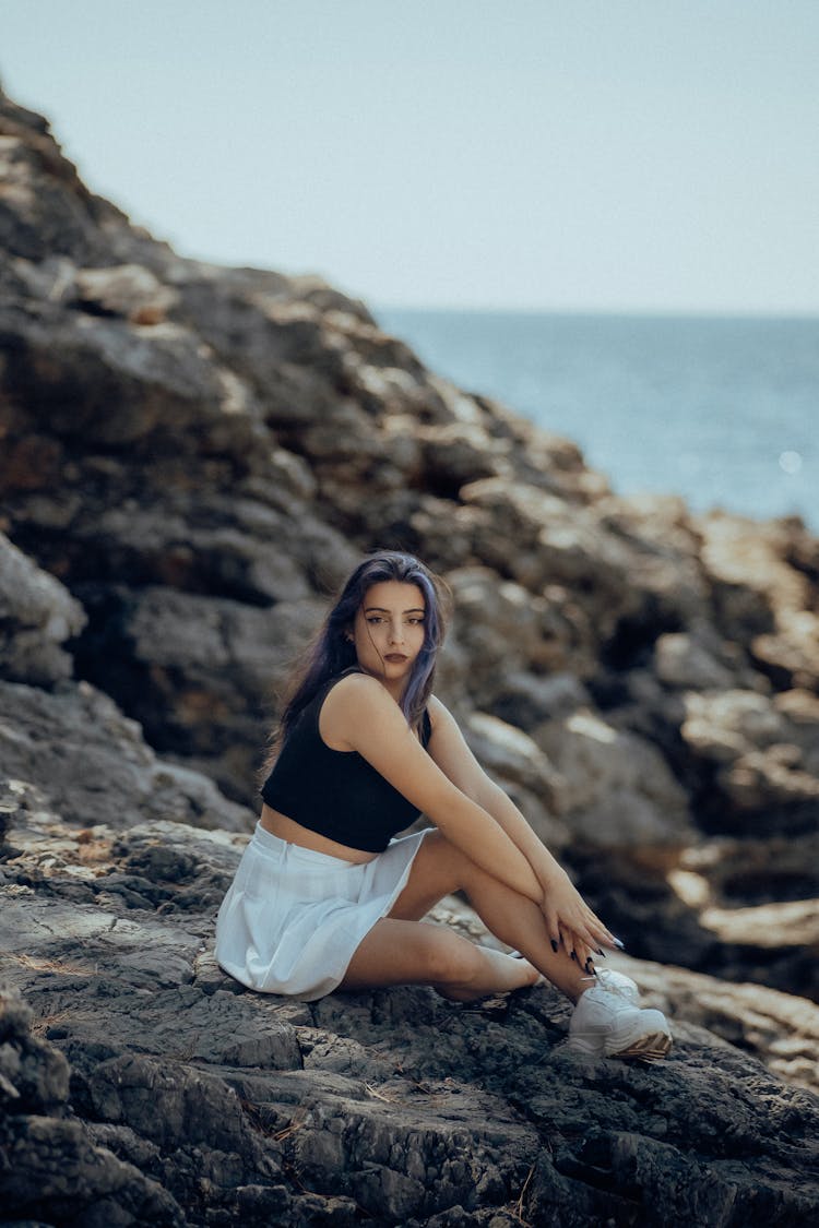 Woman Sitting On Rocks On Shore