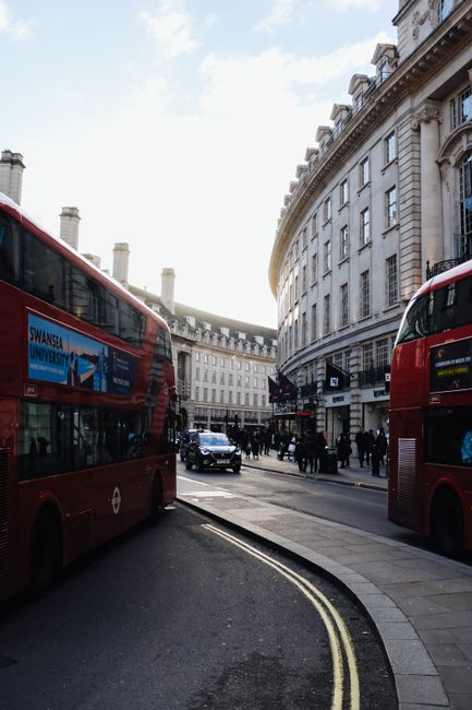 A vibrant city street in London featuring iconic red double-decker buses and historic architecture.