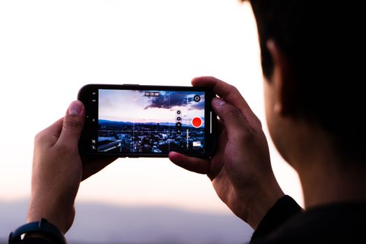 A person records a scenic sunset over Mexico City using a smartphone, capturing urban beauty.