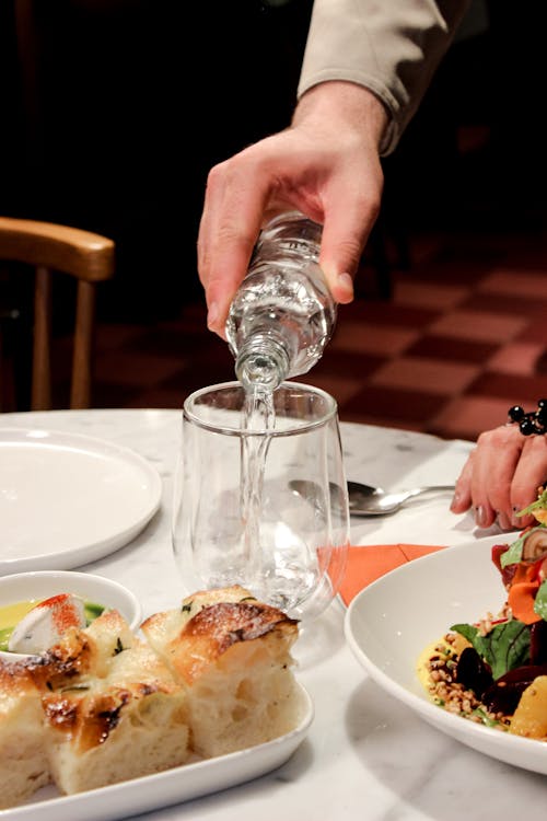 Man Pouring Water to Glass on Table