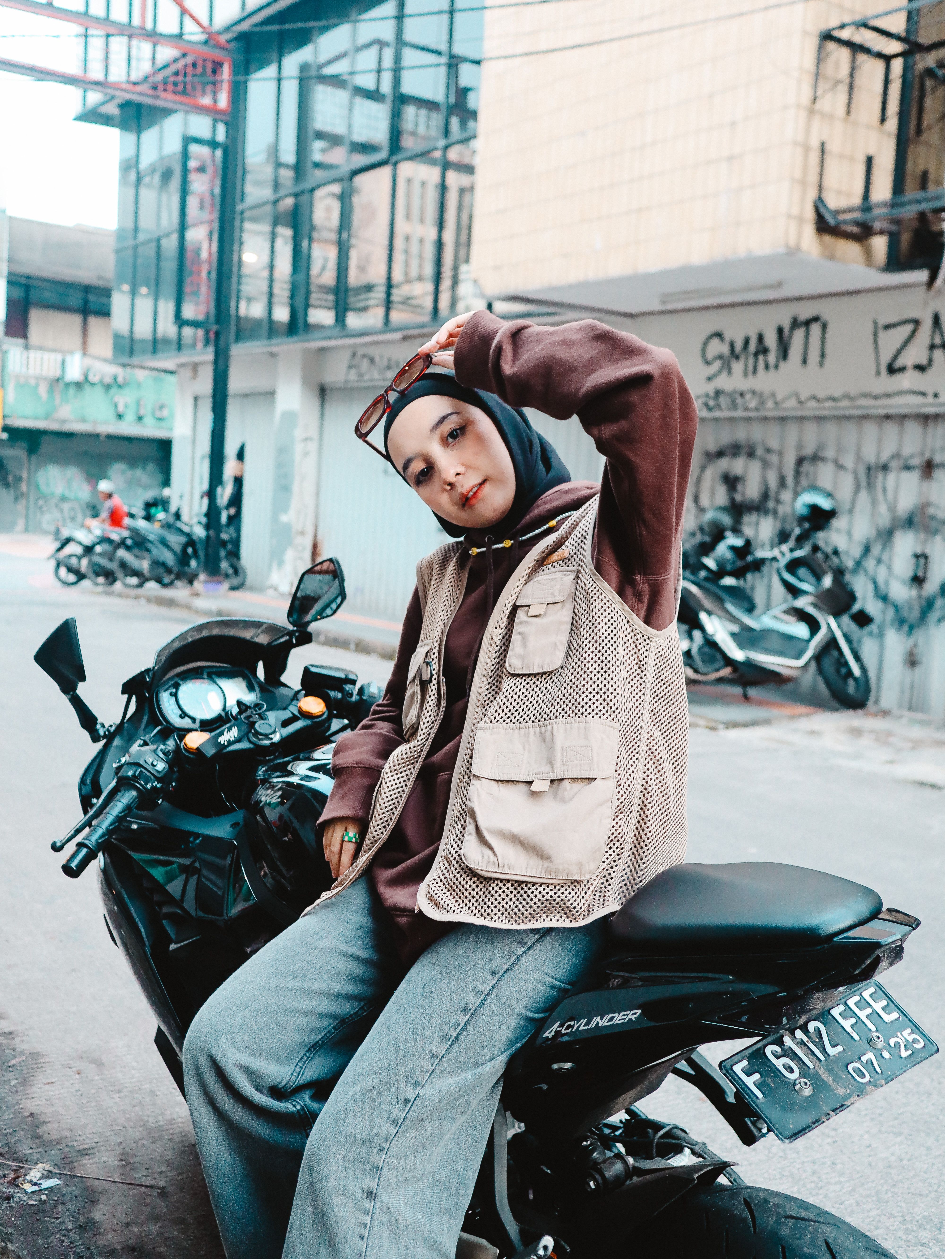 Stylish woman in hijab sitting on a motorcycle on urban city street, exuding confidence.