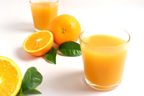 Free Close-up of Freshly Squeezed Orange Juice in Glasses and Oranges Lying on White Surface Stock Photo