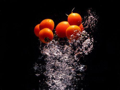Free Cherry tomatoes immersed in water with dynamic bubbles on a black background. Stock Photo