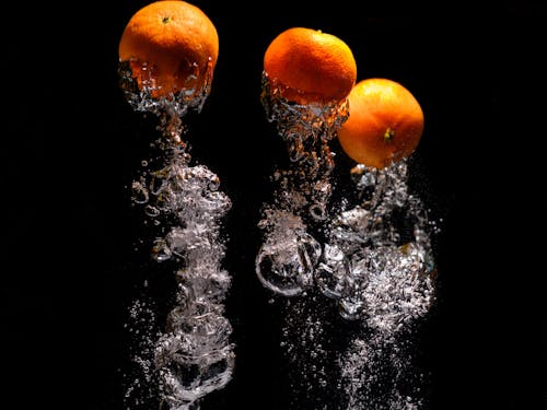 tangerines falling into water with splash on black background