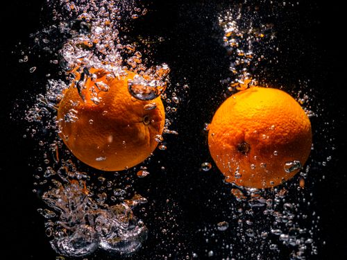 Free Two oranges creating a splash with water bubbles against a dark backdrop, showcasing freshness. Stock Photo