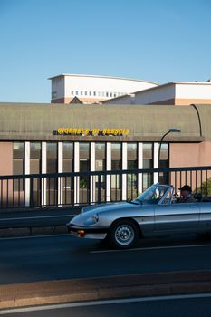 A classic Alfa Romeo Spider convertible car driving past the Giornale di Brescia building.