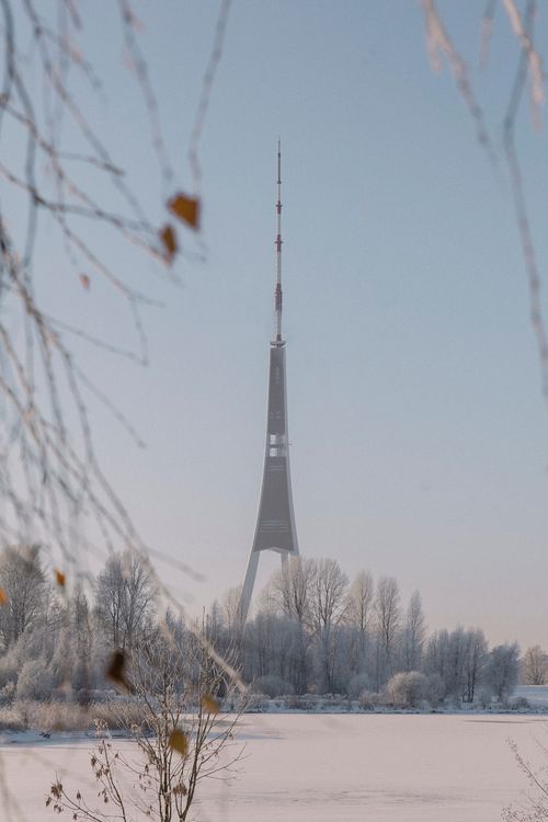 Free Vertical shot of a tall transmission tower surrounded by a snowy landscape and clear blue sky. Stock Photo