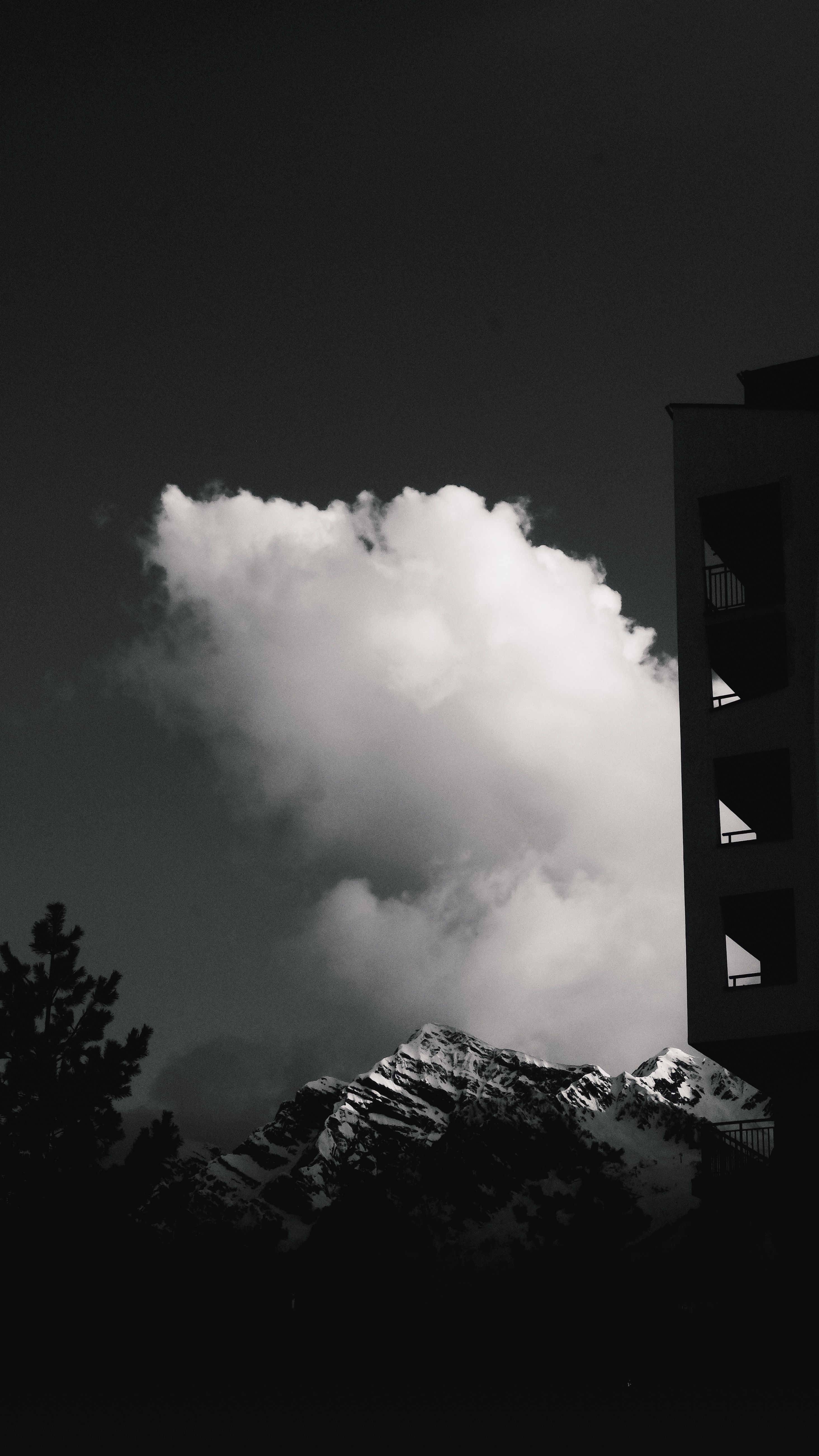A striking black and white photo of clouds over mountain peaks with building silhouette.