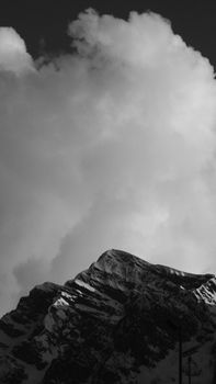 Black and white photo of a snow-capped mountain peak against a cloudy sky.