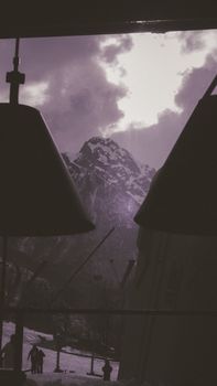 Dramatic mountain view seen through a café window with snow-covered ski slopes.
