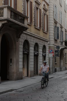 A cyclist rides through a historic cobblestone street in a European city. Tranquil urban scene.