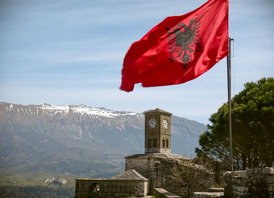 Iconic view of Gjirokaster Fortress featuring the Albanian flag and a clock tower under a blue sky.