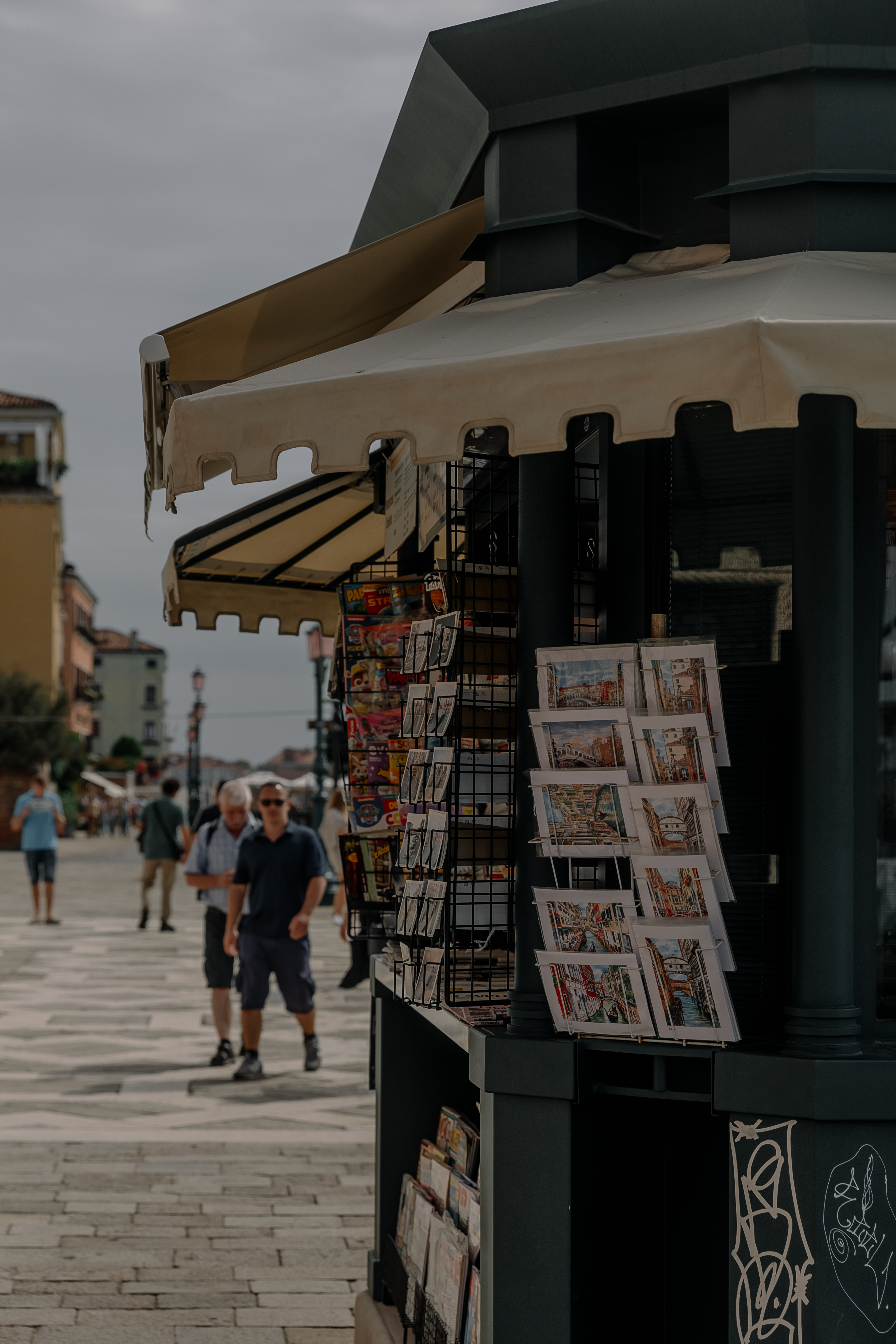 An urban souvenir stall on a bustling city street, offering postcards and more to passing tourists.