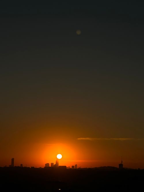 Free Dramatic urban sunset with city skyline silhouette against vibrant orange sun. Stock Photo