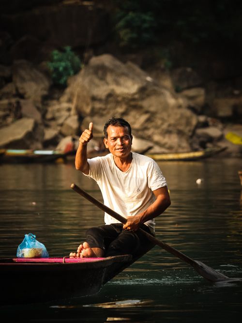 Free Smiling man paddling a boat on tranquil water with a thumbs up gesture. Stock Photo