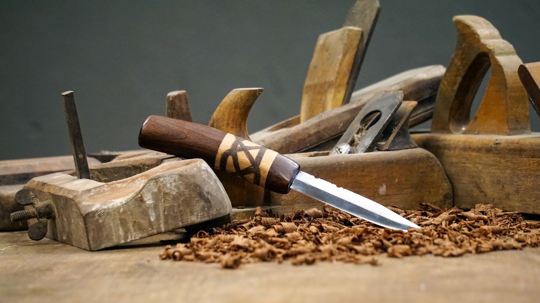 A detailed display of vintage carpentry tools and a knife on a wooden workbench shavings.