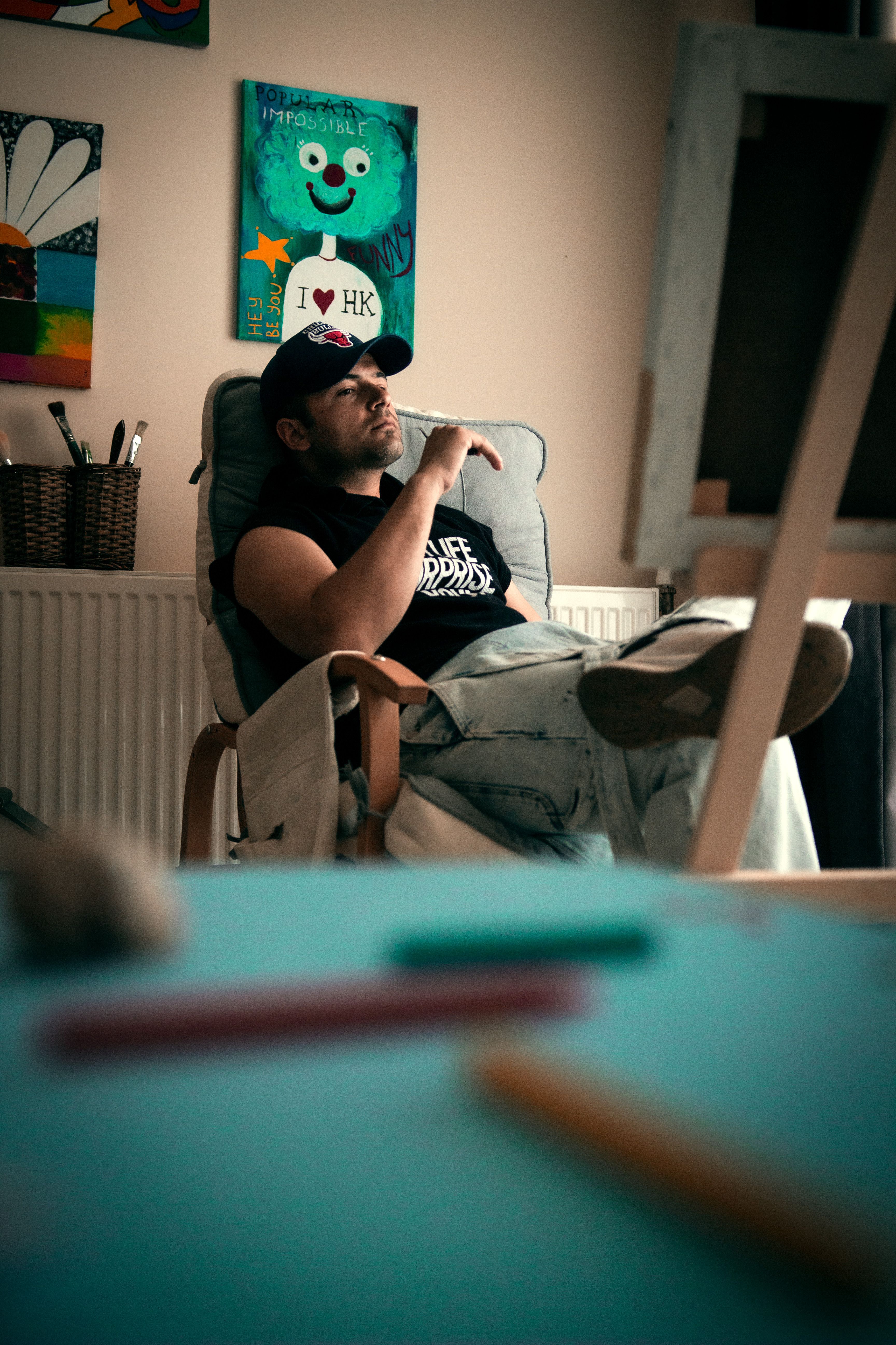 A man in a cap relaxes in an armchair in a stylish room with colorful posters.